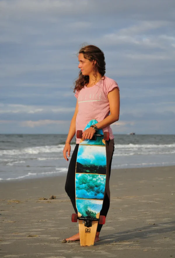 One Wave Shirt - Beach Tee Flamingo, am Strand mit Skateboard. Lässig geschnittenes Damen T-Shirt aus 100% Bio-Baumwolle.